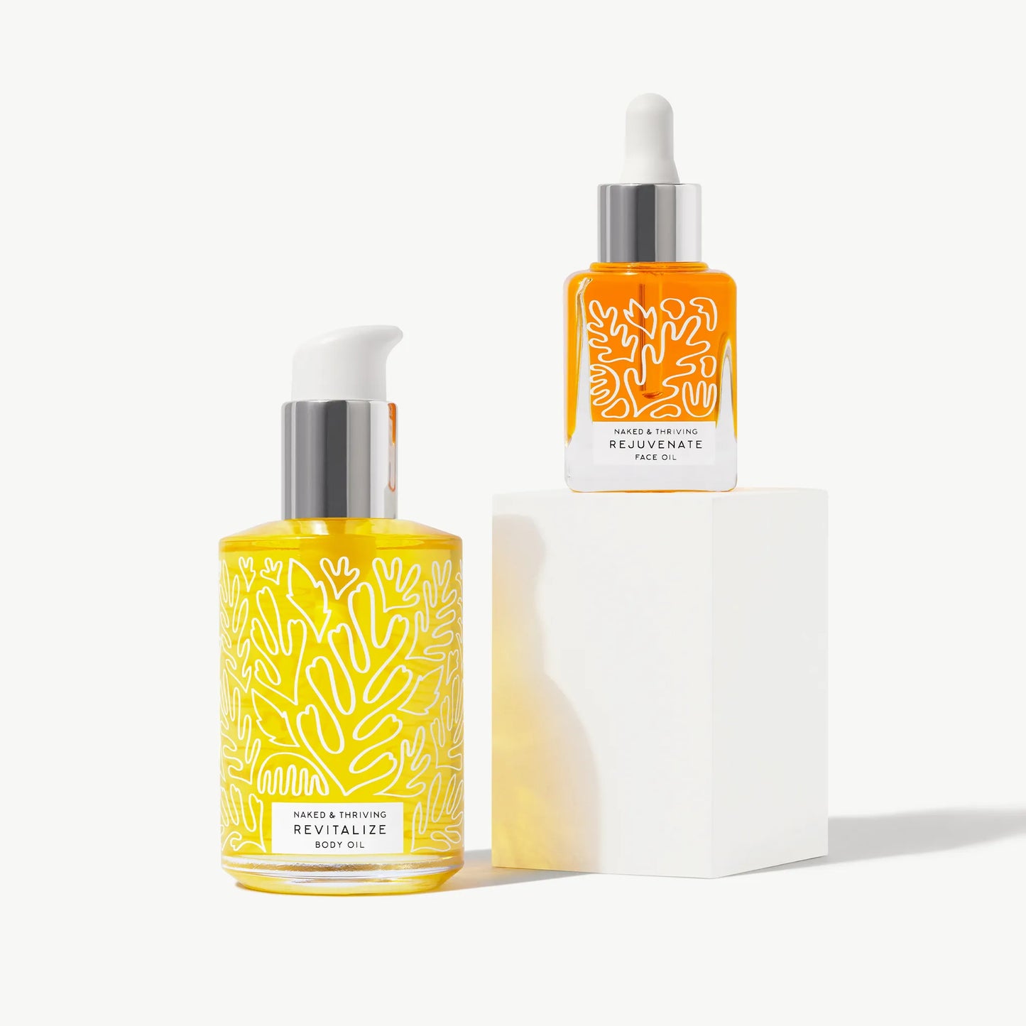 Rejuvenate face oil and Revitalize body oil bottles arranged on a light background