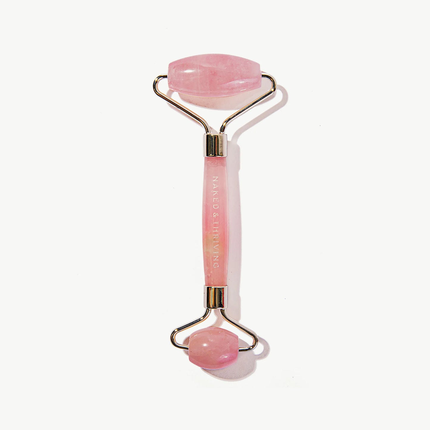 Naked & Thriving pink quartz facial roller massage tool on white background