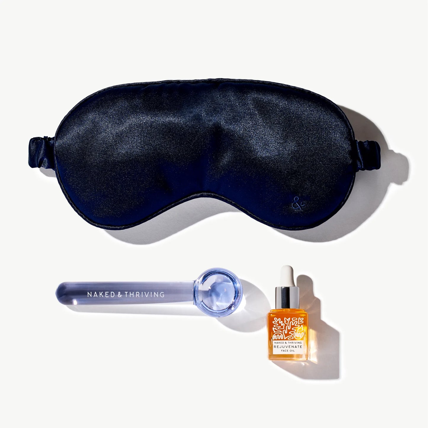Navy sleep mask, de-puffing tool, and mini face oil arranged as a set